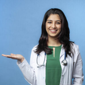 Beautiful Young Doctor Lady pointing with hand on copy space, studio shot. Isolated on a blue background